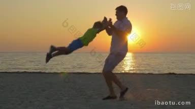 年轻的父亲和小儿子在海滩上玩耍，爸爸在大海和金色的背景上旋转孩子